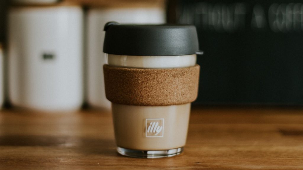 A glass to-go coffee cup with a cork sleeve.