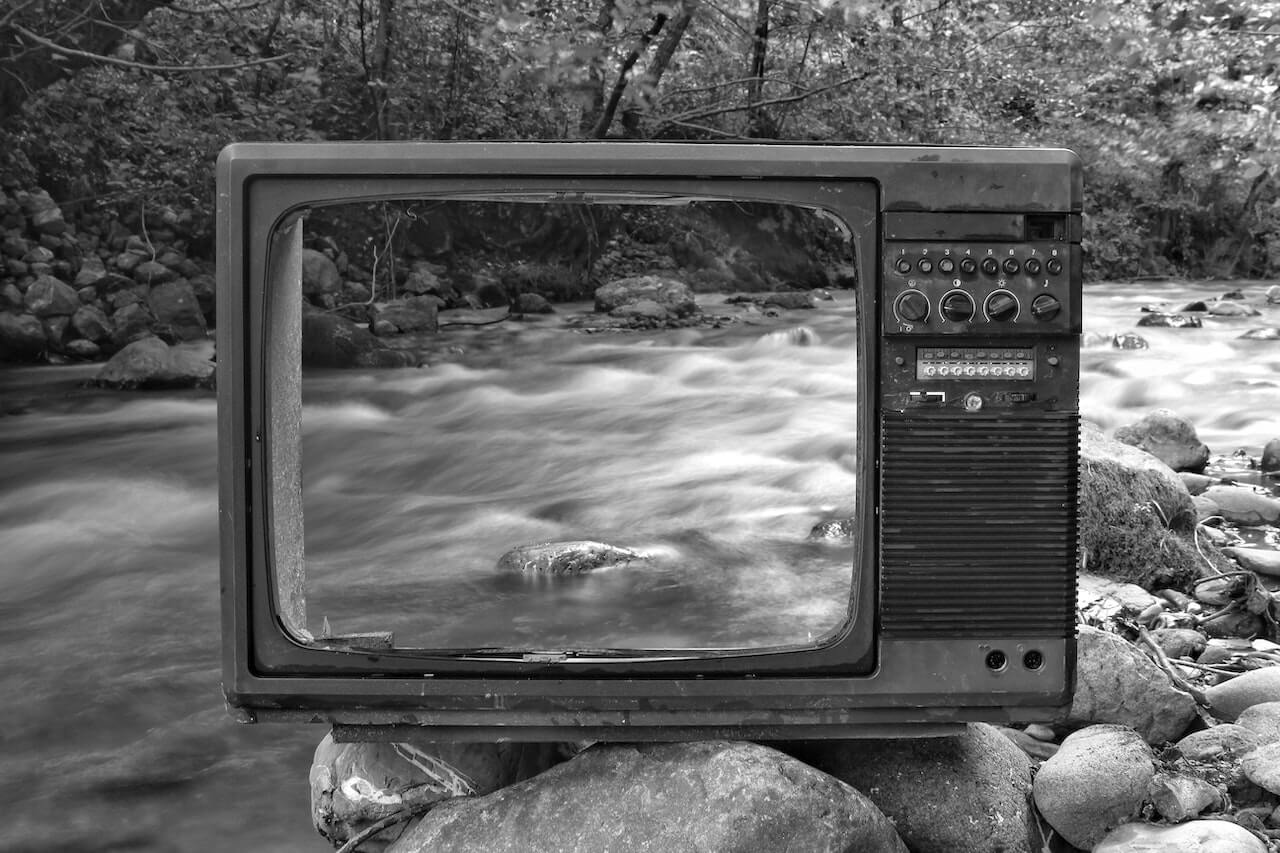 Image en noir et blanc d'un cadre de télévision creux posé sur un rocher, avec un ruisseau serein en arrière-plan.